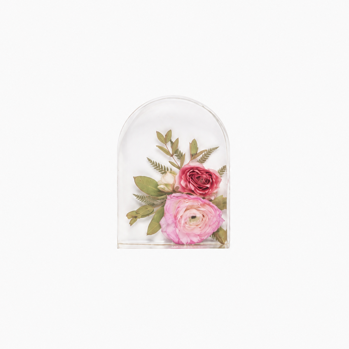 A small clear arched resin dome containing two pressed flowers, one pink and one rose pink, with green leaves, centered on a plain white background.