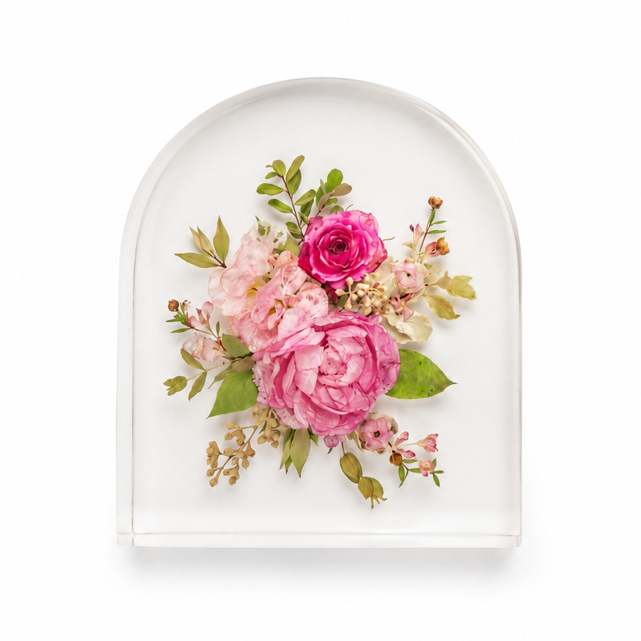 A clear arched resin plaque featuring a pressed floral arrangement with pink roses, light pink blossoms, green leaves, and small cream details, centered on a white background.