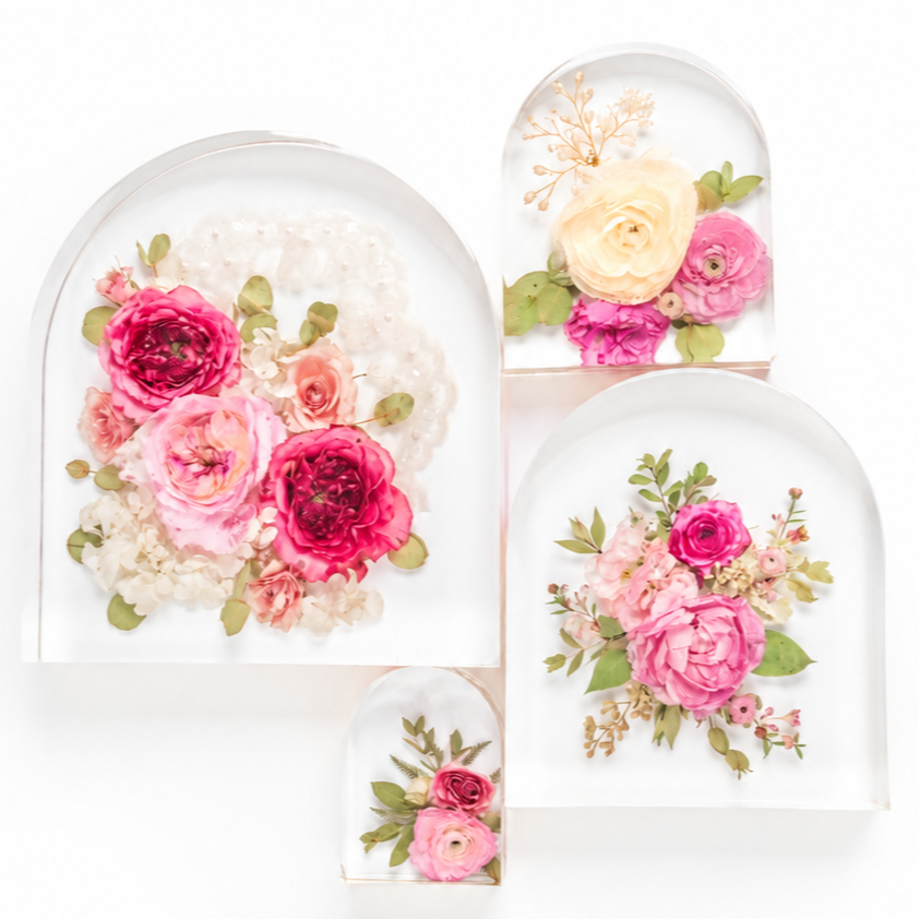 Four arched clear resin arches with preserved dried and pressed flowers in pink, cream, and green, arranged on a white background.